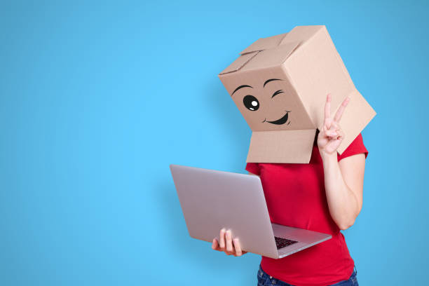 Packaging cardboard on the head with different emotions Happy person with cardboard box on its head and a happy face expression with a winking eye showing victory sign with its fingers on blue background people with boxes over their head stock pictures, royalty-free photos & images